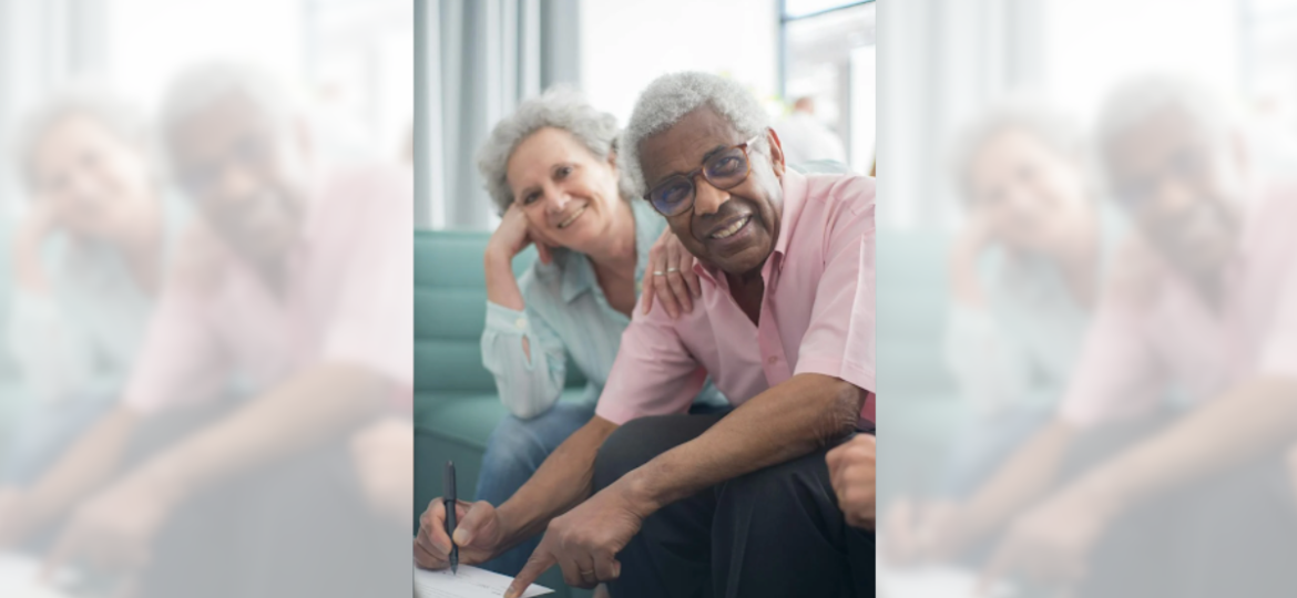 Happy retired couple smiling on couch, planning federal retirement benefits, and signing documents for the FERS Annuity Supplement.